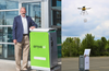 Dan O’Toole stands next to an Arrive AI smart mailbox. Beside him, a drone delivers a package into another smart mailbox in an outdoor demo of autonomous delivery.